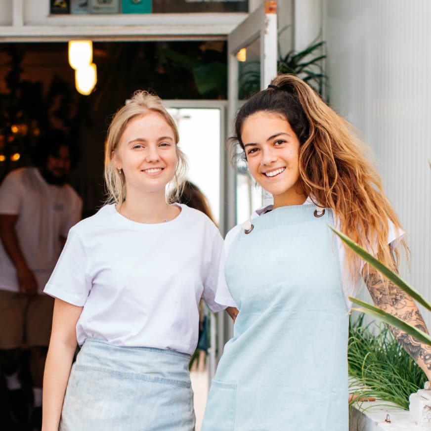 two female waitstaff standing in front of a cafe smiling