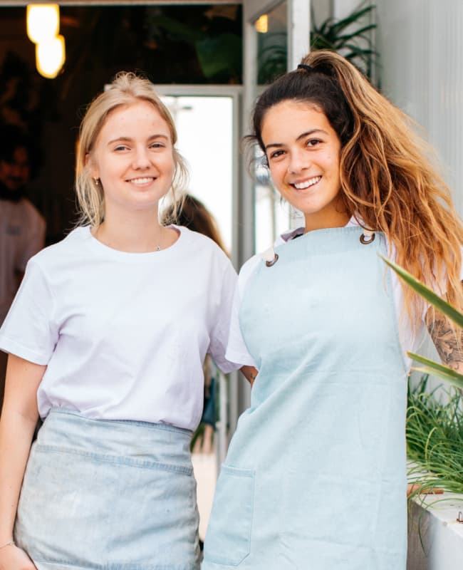 two female waitstaff standing in front of a cafe smiling